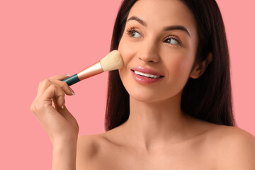 Obraz premium Beautiful young woman with makeup brush on pink background