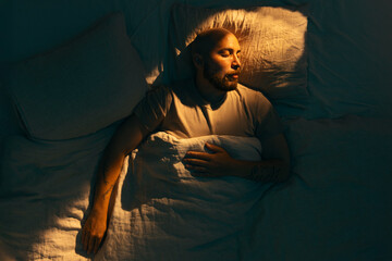 A caucasian man with a beard peacefully sleeping in bed lit by a warm morning light.