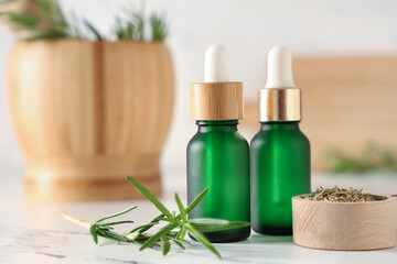 Rosemary with bottles of essential oil on light background