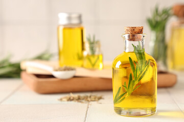 Rosemary with bottles of essential oil on white tile background