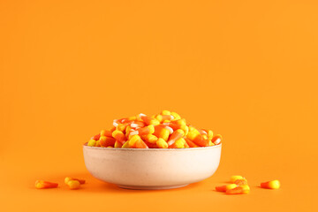 Bowl with tasty Halloween candy corns on orange background, closeup