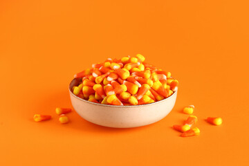 Bowl with tasty Halloween candy corns on orange background, closeup