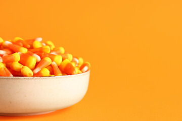 Bowl with tasty Halloween candy corns on orange background, closeup