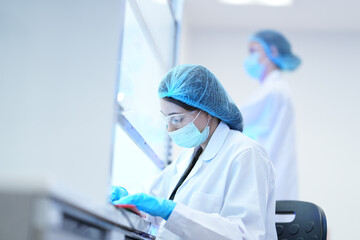 A researcher performs an aseptic technique inside a Class II biosafety cabinet. The sterile environment is critical for cell culture or virology work in a biotechnology lab.