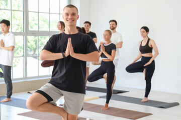 Obraz premium Sporty young man practicing yoga with group at gym