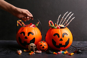 Female hand with decorative pumpkins of different sweet candies on dark background. Halloween...