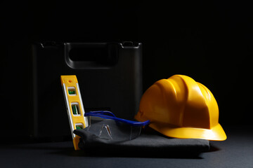 Hardhat, tool box and safety glasses on black background, closeup