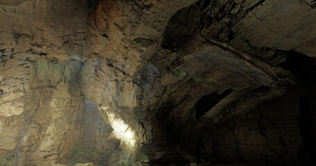 A large rock cavern reveals textured stone walls, with patches of light highlighting the natural formations and shadows. The atmosphere is tranquil and mysterious.