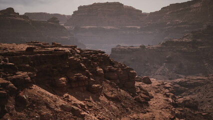 In a stunning desert environment, towering canyon walls rise above rocky terrain, bathed in warm hues as the sun sets, showcasing natures beauty and rugged formations.