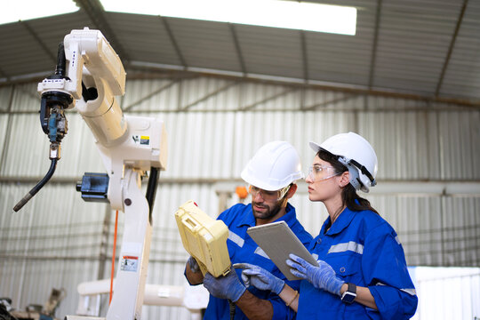 Blue collar workers at machine shop with welding robot arm.