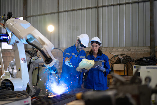Blue collar workers at machine shop with welding robot arm.