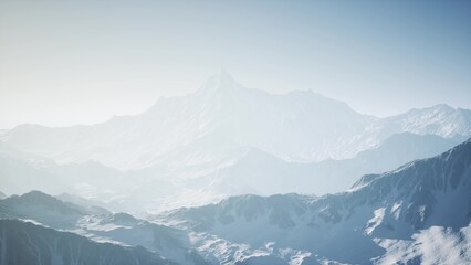 Fototapeta premium Vast mountain landscape emerges from gentle mist as dawn breaks. The soft light unveils snow capped summits and rugged terrain, evoking a sense of peace and wonder.