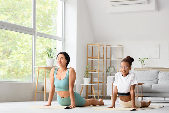 African-American mother with her teenage daughter practicing yoga on mats at home - Powered by Adobe