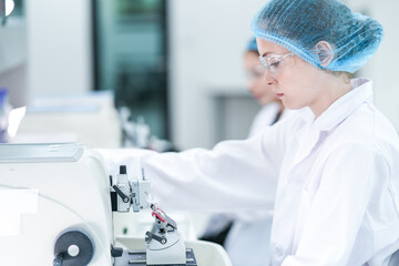 Female medical laboratory technologists in full protective gear work efficiently in a row, operating specialized equipment to process biological samples in a bright, modern clinical lab.