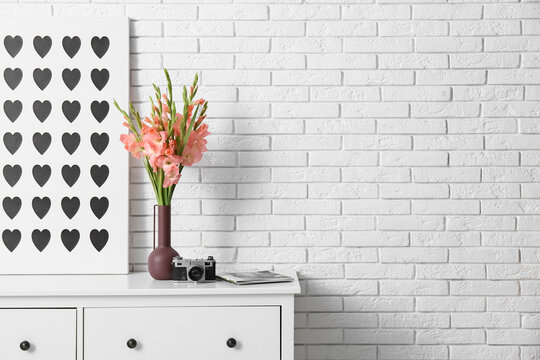 Picture, photo camera and vase with beautiful gladiolus flowers on chest of drawers in living room, closeup