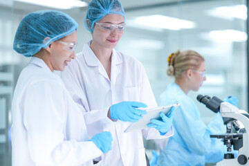 A senior scientist mentors a junior researcher, pointing at results on a digital tablet as they...