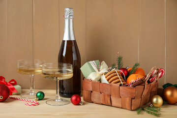 Gift basket with products, Christmas decor, glasses and bottle of champagne on beige wooden background