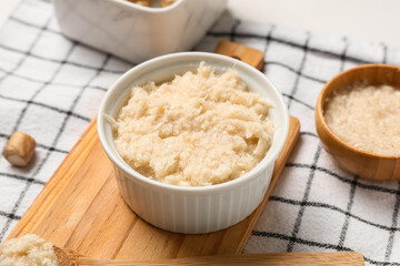 Wooden cutting board and bowl with horseradish sauce on napkin as background, closeup