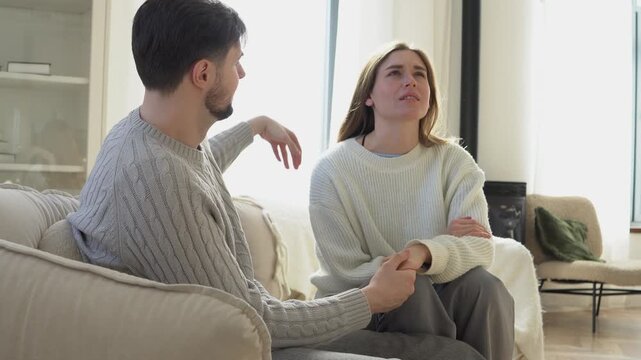 young couple in relationship are sitting on the couch at home and talking, the husband is listening to his wife, calming her down and supporting her