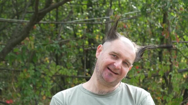 A bald man with unusual pointed hairstyle and beard shakes his head playfully outdoors, making comic expressions. Funny hairstyle humor video.
