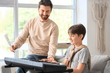 Cute boy learning to play synthesizer with private music teacher at home