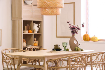 Vase with eucalyptus branches, pumpkins and dishes on dining table in room