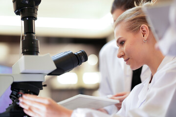 A team of medical researchers discusses their experiment's results. They are analyzing data and microscope findings together in a clinical laboratory to reach a conclusion.