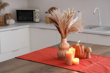 Vase with pampas grass, autumn decor and burning candles on dining table in kitchen