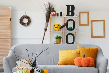 Interior of light living room decorated for Halloween with grey sofa, shelf unit and broom