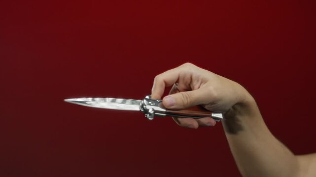 Man holding knife against red background showcasing sharp blade and firm grip in isolated setting emphasizing safety and caution.