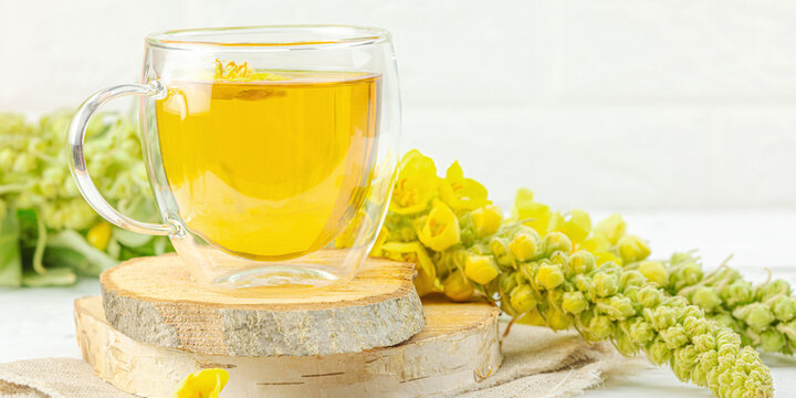 Glass cup of mullein herbal tea on natural wooden background with fresh Verbascum thapsus flowers
