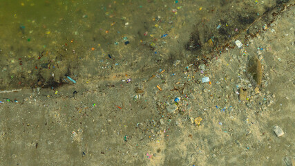 A sandy beach severely polluted with a large accumulation of plastic bottles and other trash. ocean...