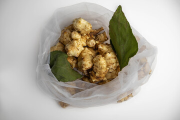Jerusalem artichoke with green leaves in an eco bag on a white background.