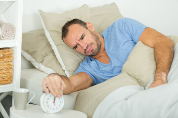 young man turning off the alarm clock on the bed