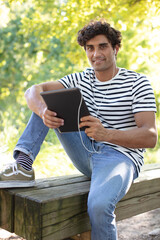 Fototapeta premium young man outdoors listening to music using tablet and earphones