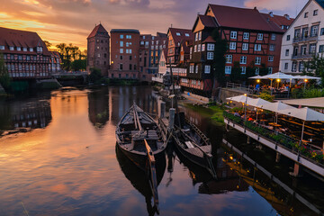 Historic waterfront buildings with moored wooden boats reflecting in sunset light