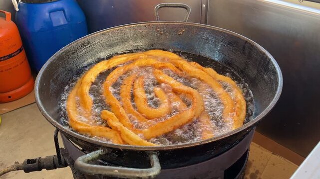 Golden churros frying in hot oil in a large pan