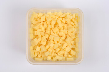 An overhead shot features a transparent, square container completely filled with yellow cheese cubes, centered on a plain white background
