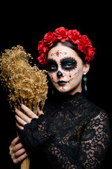Halloween beauty portrait of female adorned with Santa Muerte makeup. Bouquet of dry grass in his hands.