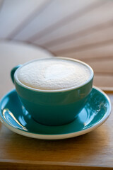 A teal ceramic cup with heart-shaped latte art 
