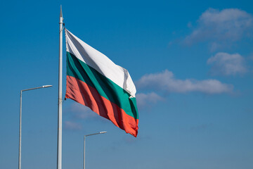 The Bulgarian national flag waves proudly against a clear blue sky, symbolizing identity and unity in a public outdoor setting.