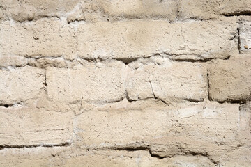 A close-up shot of an old, weathered brick wall covered in rough, light beige stucco or plaster