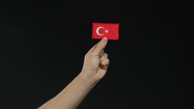 Man holding turkish flag patch against dark background.