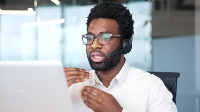 African american businessman in a headset talking on a video call using laptop sitting in office. Entrepreneur has a business meeting. The manager speaks remotely at an online conference. Close up