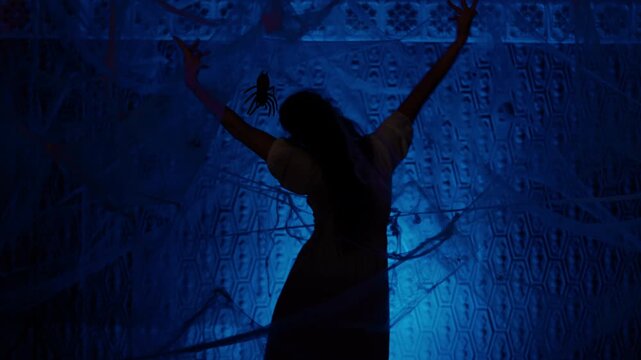 silhouette of female dancer performing creative dance on stage surrounded by thick spider web illuminated with mystical blue light.