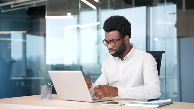 Frustrated african american businessman having difficulty making transaction using laptop while sitting at workplace in business office. Confused male worker having problems working online on computer