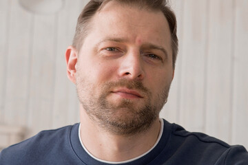 Obraz premium Handsome young man in blue jersey indoors. Male with stylish haircut, beard feel happy, calm and serious. Home interior background. Man looking to camera and into distance. Diversity People. Portrait