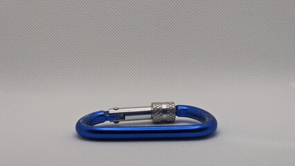 Carabiner biru berbahan logam dengan kunci pengaman, diletakkan di atas latar polos abu-abu. Cocok...