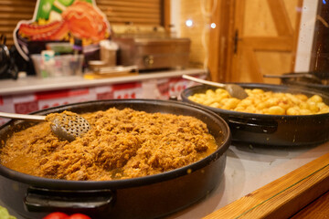 Traditional Polish bigos with meat in large pan and potatoes in another pan at Christmas market. Concept of festive cuisine, tradition and European street food