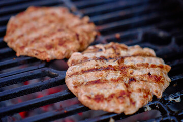 Two meat patties cooking on hot barbecue grill with visible grill marks. Concept of food, barbecue and outdoor cooking.